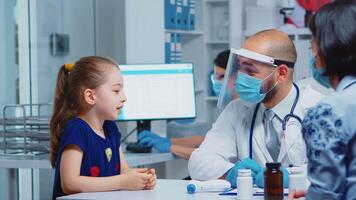 Doctor talking with child wearing protection mask during coronavirus. Pediatrician specialist in medicine providing health care services, consultation, treatment, examination in hospital cabinet. video