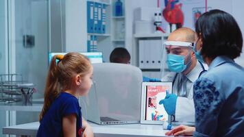 Physician talking about heart functions with patients during coronavirus using tablet. Pediatrician doctor in protection gloves and mask providing clinic medicinal health care services consultation treatment video