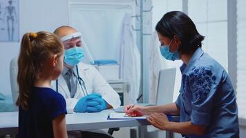 Woman writing prescription on clipboard listening doctor instructions. Pediatrician specialist in medicine with mask providing health care services, consultation, treatment in hospital during covid-19 video