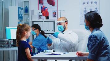 Doctor examining girl by stethoscope in medical office during the pandemic. Pediatrician specialist in medicine with mask providing health care services, consultation, treatment in hospital cabinet. video