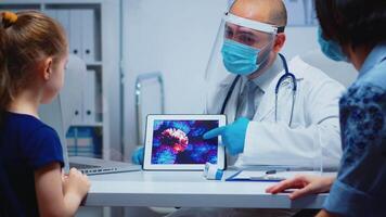 Doctor explaining evolution of virus wearing protection mask using tablet. Pediatrician specialist with visor and gloves providing health care services, consultations, treatment during coronavirus. video