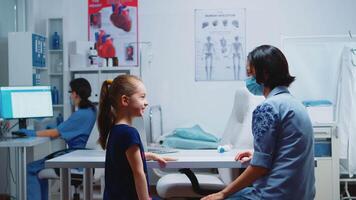 mãe e filha falando e esperando para a médico dentro médico escritório durante coronavírus. especialista dentro remédio com proteção mascarar fornecendo saúde Serviços, consulta, tratamento dentro hospital. video