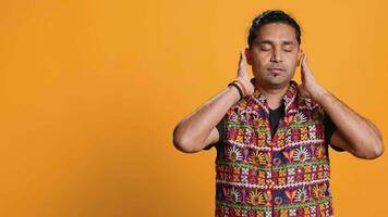 Man wearing traditional indian clothing covering eyes, ears and mouth, imitating three wise monkeys, doing dont see, dont hear and dont speak hand gesturing concept, studio background, camera A video