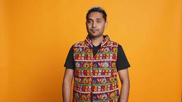 Portrait of jolly indian man with colorful garment smiling, looking pleased, isolated over studio background. Joyous person in traditional attire feeling carefree, camera B video