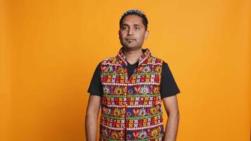 Portrait of optimistic indian man wearing colorful vest with positive facial expression smiling, looking pleased. Calm person in traditional clothing, feeling satisfied, studio backdrop, camera B video