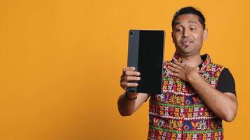 Radiant man saluting friend over online videocall, doing friendly gestures. Joyful person communicating with mate on teleconference using tablet, studio background, camera A video