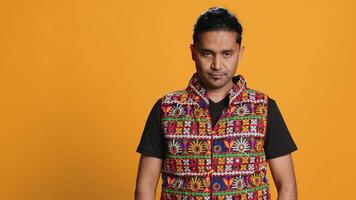 Portrait of optimistic indian man wearing colorful vest with positive facial expression smiling, looking pleased. Calm person in traditional clothing, feeling satisfied, studio backdrop, camera A video