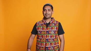 Portrait of jolly man smiling and waving hand, saluting, gesturing, isolated over studio backdrop. Joyous upbeat indian person in traditional attire doing greeting hand gesture, camera B video