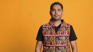 Portrait of cheerful friendly indian man smiling, looking pleased, isolated over studio background. Happy expressive asian person in traditional attire grinning, feeling satisfied, camera A video