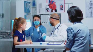 Nurse with visor and gloves giving pills to doctor. Pediatrician specialist in medicine with protection mask providing health care service consultation examination in hospital cabinet during covid-19 video