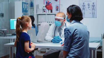 Medical specialist examining child x-ray in hospital during pandemic. Pediatrician doctor with protection mask providing health care services, consultation, radiographic treatment in medical office. video