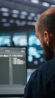 Vertical System administrator running script on computer screen in high tech data center, ensuring optimal performance. Worker monitoring energy consumption, doing checkup on server rackmounts clusters video