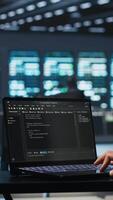 Vertical IT support employee writing code on laptop in high tech facility with server rows providing computing resources for different workloads. System administrator uses notebook to oversee supercomputers video