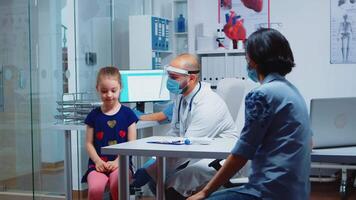 Pediatric physician with protection mask and stethoscope listening breath of girl. Doctor specialist in medicine providing health care services, consultation, treatment during covid-19 in hospital video