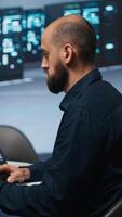 Vertical Man in server room typing code on laptop and PC, ensuring data remains shielded from threats. IT expert using notebook and computer to protect supercomputers against unauthorized access video