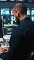 Vertical Computer scientist using laptop device to do programming in data center room housing servers . IT supervisor writing code on notebook to mend data storage facility racks doing computational operations video