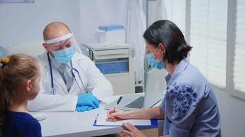 Mother writing on clipboard doctor instructions wearing protection mask. Physician specialist in medicine providing health care services consultation treatment examination in hospital during covid-19 video