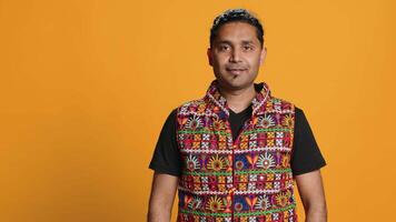 Portrait of jolly man smiling and waving hand, saluting, gesturing, isolated over studio backdrop. Joyous upbeat indian person in traditional attire doing greeting hand gesture, camera A video