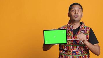 Upset indian man shows thumbs down sign gesturing holding isolated screen tablet, disapproving. Person does rejection hand gesture regarding mockup device, studio background, camera A video