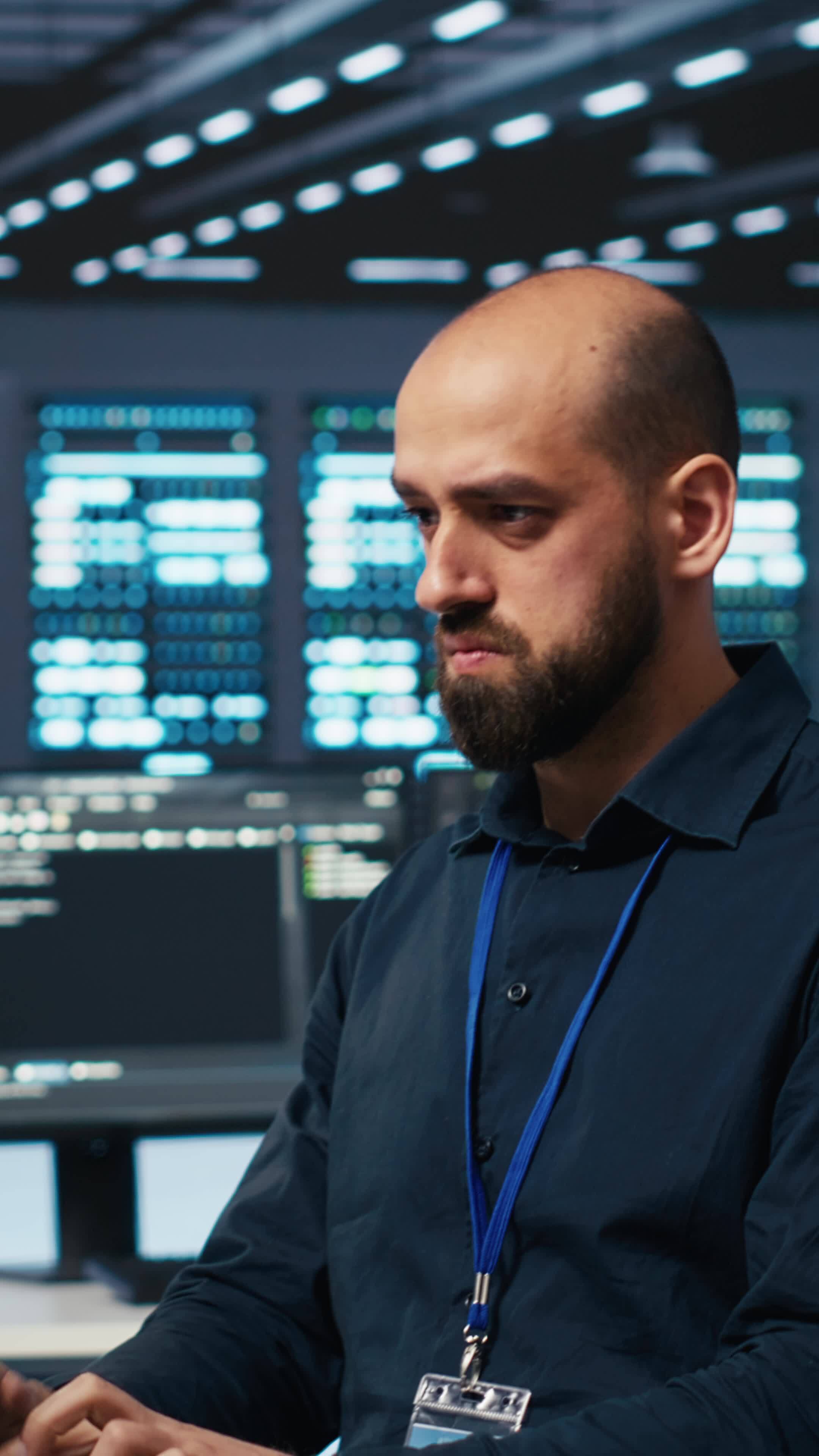 Vertical System operator overseeing server room, typing code on desktop ...