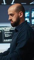 Vertical IT engineer overseeing server room, running code on computer, troubleshooting servers. Programmer at work upgrading hardware clusters, networking systems and storage arrays video