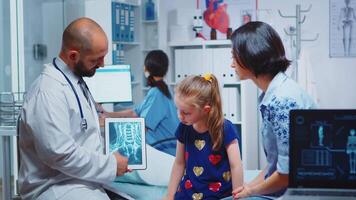 Male pediatrician checking bone X-ray on tablet in clinic. Healthcare practitioner physician specialist in medicine providing health care service radiographic treatment examination in cabinet hospital video