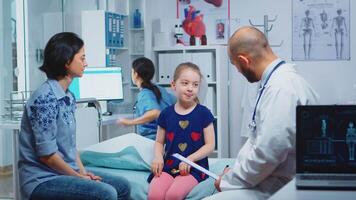 Doctor talking with little girl sitting on bed in medical office Healthcare practitioner, physician, specialist in medicine providing health care services consultation diagnostic treatment in hospital video