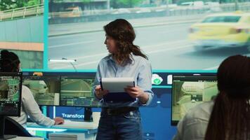Portrait of woman supervisor overseeing the traffic surveillance monitoring activity in a observation room, CCTV satellite system. Diverse team of people handling license plate reading. Camera A. video