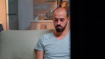 Tired man working on project for internet communication using laptop computer sitting on sofa. Freelancer writing information while standing in front of television late at night in living room video