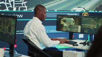 Operator uses satellite navigation map to guide delivery truck drivers, works in observation room to avoid traffic. African american employee tracing orders within the surveillance system. Camera A. video
