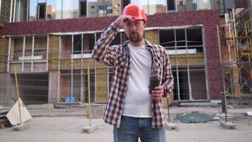 Young caucasian male foreman builder tired and drinks coffee on background construction site. Engineer in protective equipment coffee break. Construction inspector drinks hot drink after hard day. video