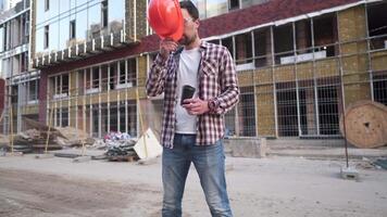 Engineer builder having coffee break at construction site. Caucasian man with takeaway coffee cup and protective gear has break while working on site. Construction worker drinking coffee. video