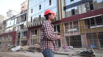 retrato masculino trabajador en naranja difícil sombrero durante descanso a construcción sitio. hombre ingeniero sostener para llevar café taza fuera de construcción sitio en naranja difícil sombrero. superintendente café descanso después difícil día video