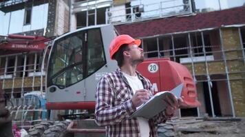 mayo 12, 2021. Ucrania. Kyiv industrial trabajador revisando planes construcción trabajador participación proyecto documentos cerca excavadora a construcción sitio. construcción ingeniero explorar documentación. video