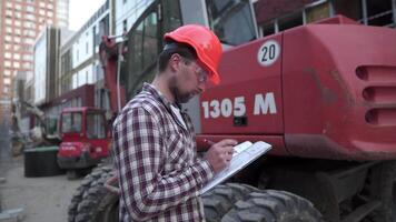 industrial trabalhador revendo planos. construção trabalhador segurando projeto documentos perto uma escavadora às uma construção local. construção gerente, engenheiro explorar construção documentação. video