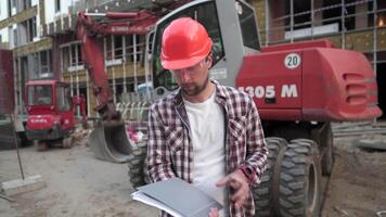 Industrial worker reviewing plans. Construction worker holding project documents near a bulldozer at a construction site. Construction manager, engineer explore construction documentation. video