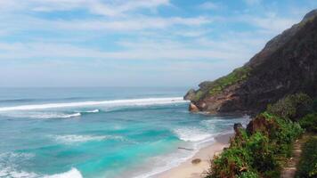 toneel- tropisch strand met rots klif en blauw oceaan met surfing golven video