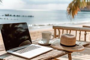 A laptop is open on a table next to a straw hat and a cup photo