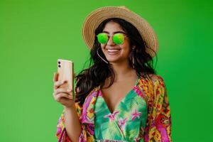 un mujer es participación un célula teléfono y sonriente. ella es vistiendo un vistoso floral vestido. concepto de felicidad y positividad foto