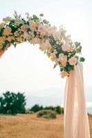 Corner of a wedding arch decorated with flowers and fabric standing in a clearing photo