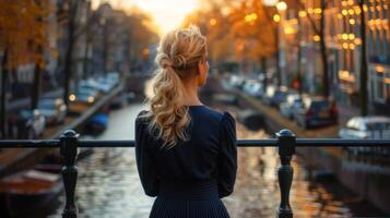 A woman in a blue dress stands on a bridge overlooking a canal photo