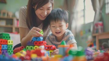 Asian young boy is playing with a stack of colorful blocks while his mother watches photo