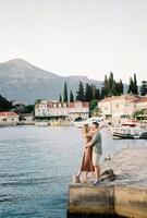 Man and woman stand hugging and almost kissing on the pier of the ancient village of Rose. Lustica, Montenegro photo