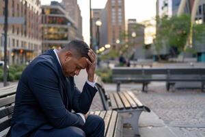 A man in a suit is sitting on a bench and looking down. He is in a state of distress or sadness photo