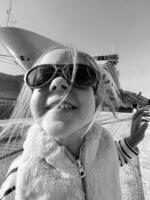 Little girl in sunglasses on the background of a large boat. Black and white photo
