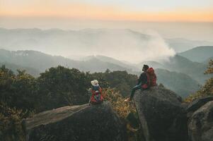 Two people are sitting on a rock in the mountains photo