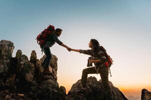 hombre y un mujer son Ayudar cada otro escalada un montaña foto