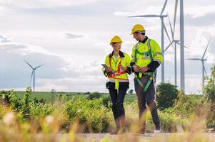 Two workers in safety gear are walking through a field of wind turbines photo