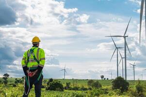 man in a yellow helmet stands in a field of wind turbines photo