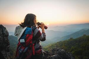 hembra turista en parte superior de montaña utilizar prismáticos a ver montaña rango a puesta de sol foto